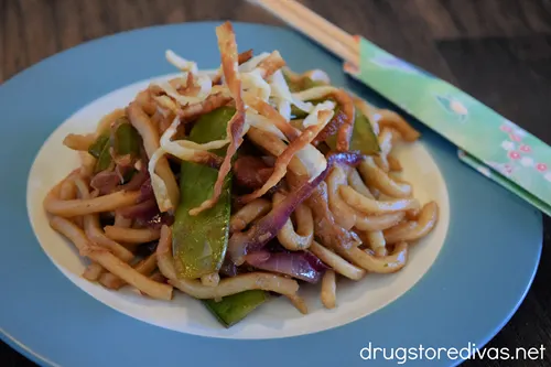 Yaki udon on a blue and white plate with chopsticks off to the side.