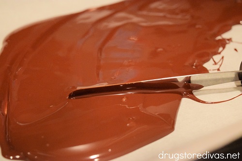 Melted chocolate on a piece of parchment paper being spread with a knife.