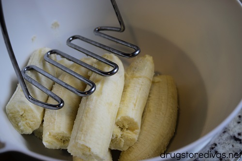 Bananas in a bowl being mashed with a potato mashed.