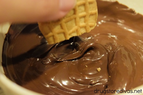 A hand dipping a cut Nutter Butter cookie into melted chocolate.