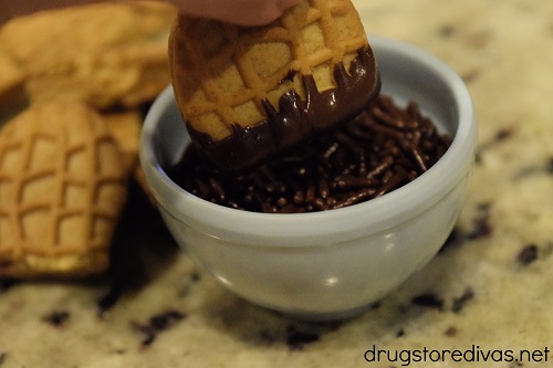 A Nutter Butter cookie half being dipped into a bowl of chocolate sprinkles.