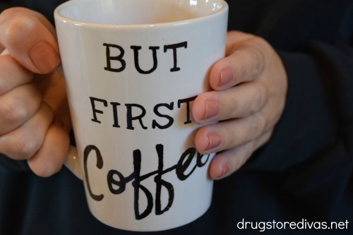 A DIY But First Coffee mug held by two hands.
