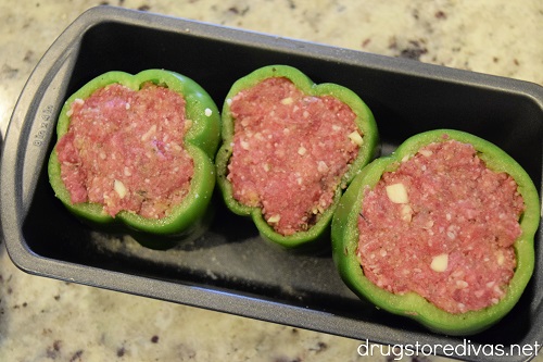 Three green peppers stuffed with a meatball mixture in a bread pan.