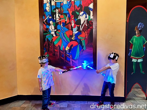 Two boys playing with light up swords in front of a painting on knights at Medieval Times.