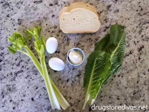 Two pieces of celery, two eggs, two pieces of bread, two pieces of Romaine lettuce, and mayo in a bowl on the counter.
