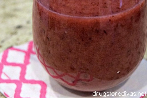 A maroon smoothie in a glass on top of a white and pink napkin.