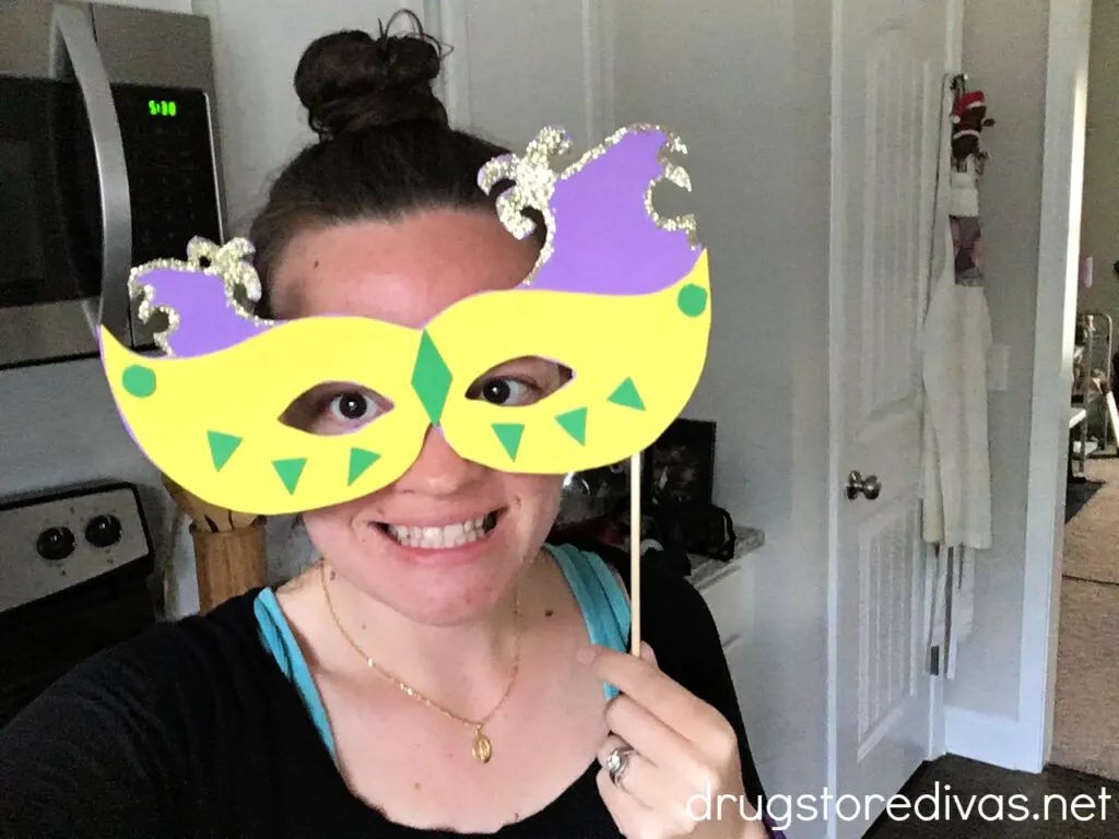 A woman holding a DIY Mardi Gras Mask over her face.