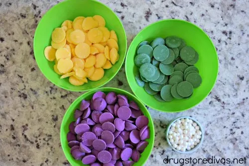 Yellow, green, and purple candy melts in bowls next to a bowl of white sugar pearls.