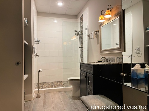 A hotel bathroom where you can see the shower in the back and vanity with sink and mirror on the side.