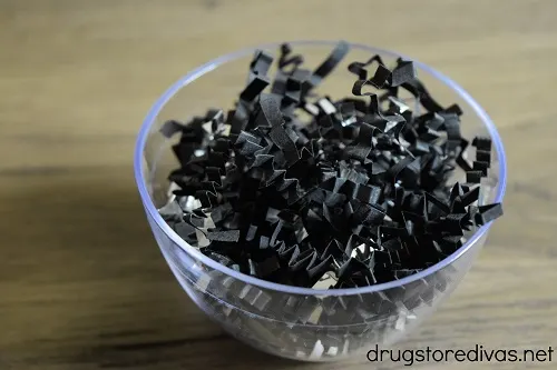 A mini plastic bowl filled with black and silver paper shred.