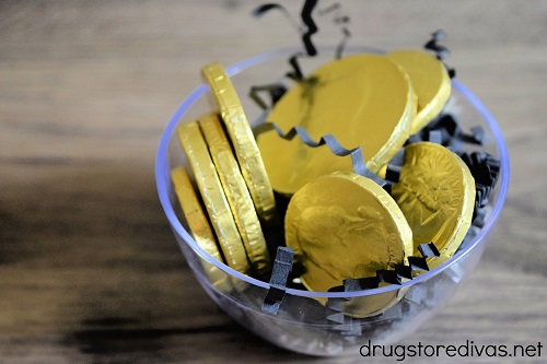 Gold coins on top of black paper shred in a clear bowl.