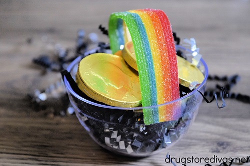 A rainbow Air Head candy shaped like a handle in a mini bowl that's filled with gold chocolate coins and black paper shread.
