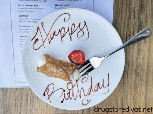 A mini cannoli with a strawberry on a plate that has Happy Birthday written in chocolate on it.