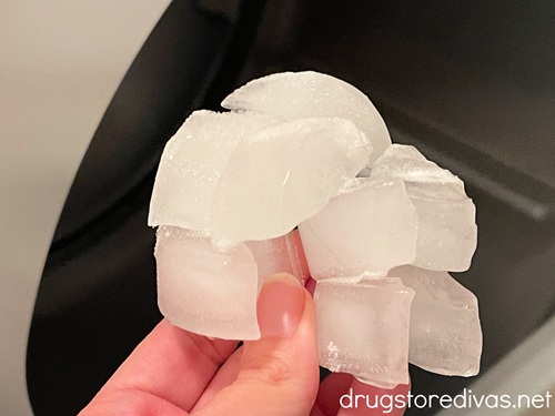 A hand holding a clump of ice cubes in front of a dryer.