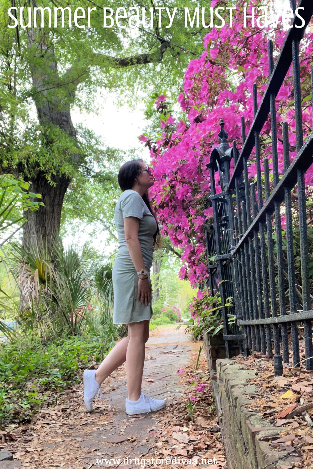 A woman in a blue dress smelling pink azalea flowers while standing on a street with the words 