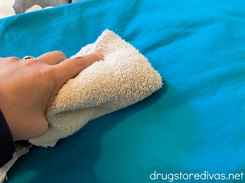 A white washcloth in a hand on top of a bright blue shirt.