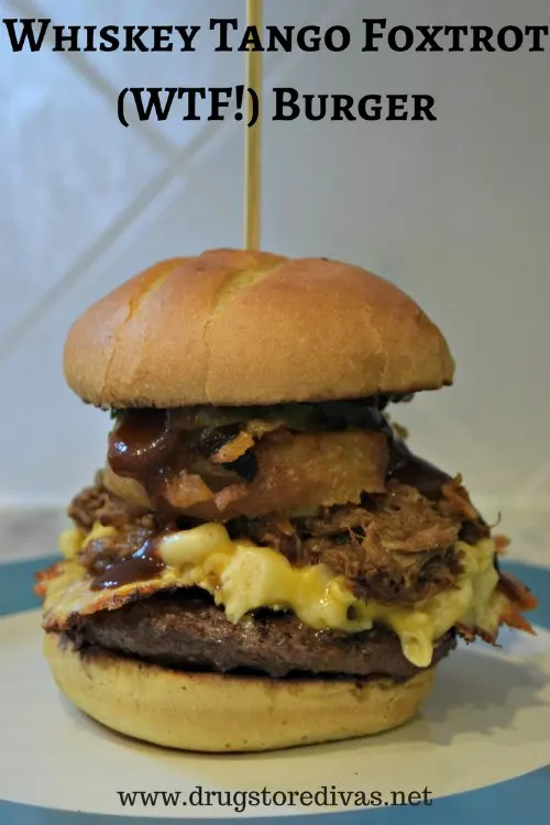 A burger with onion rings, mac and cheese, and pulled pork with the words "Whiskey Tango Foxtrot (WTF) Burger" digitally written above it.