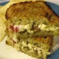 A Caprese Grilled Cheese sandwich on a plate with chips and the words 