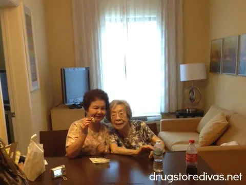 Two women in a hotel room with a couch and lamp behind them.