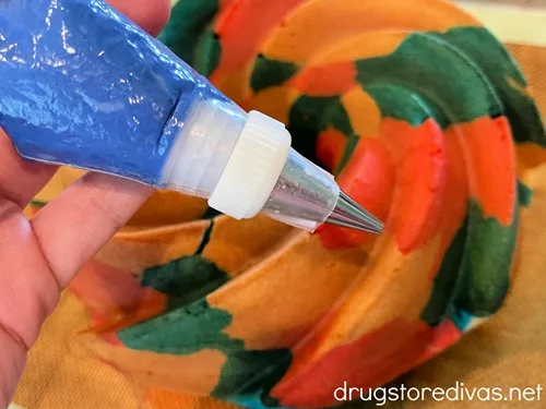 A piping bag filled with blue chocolate being held by a hand over a red, white, and blue Bundt cake.