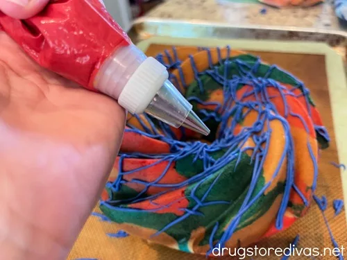 A piping bag filled with red chocolate being held by a hand over a red, white, and blue Bundt cake.