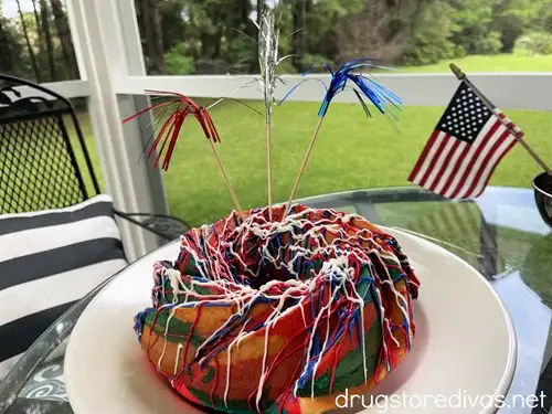A red, white, and blue Bundt cake on a white plate with metallic skewers sticking out of the top.