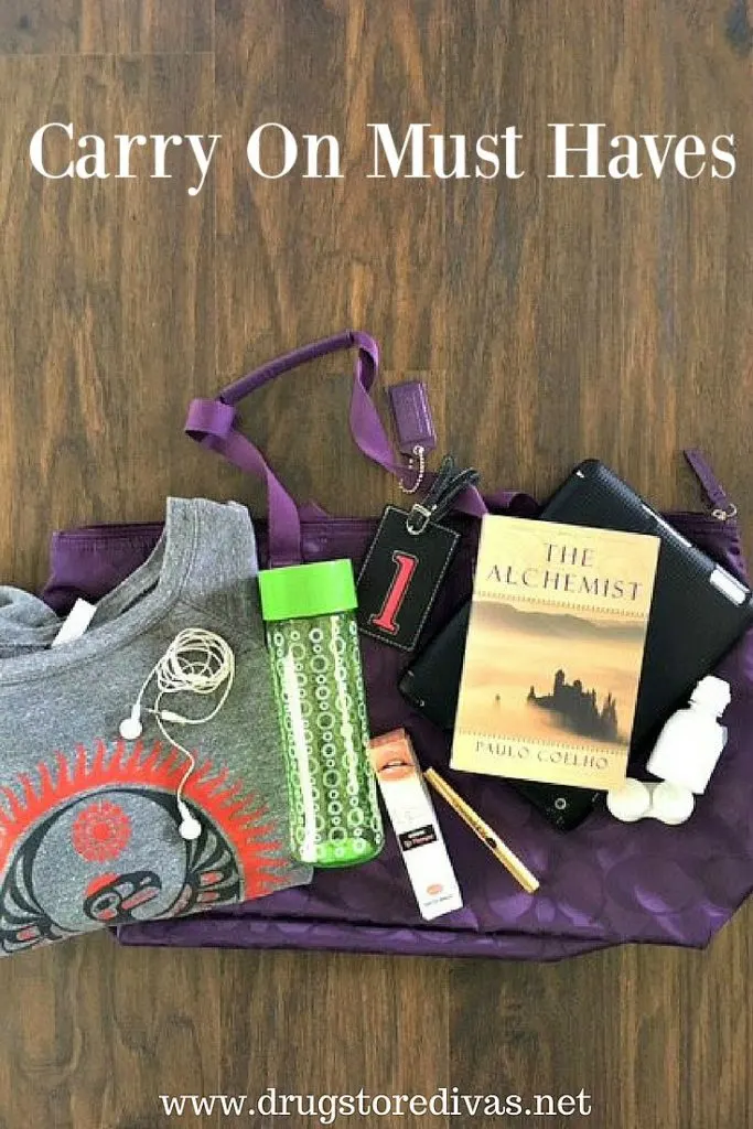 A carry on bag with a shirt, headphones, water bottle, makeup, a book, contact case and solution on it, with the words "Carry On Must Haves" digitally written on top.