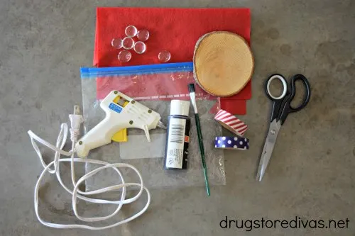A glue gun, plastic bag, red felt, wooden coaster, black paint, paint brush, Washi tape, and scissors.