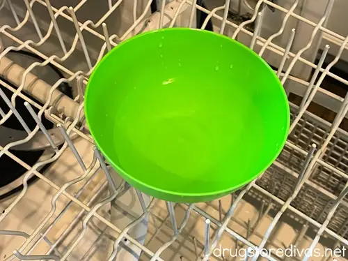 A green bowl filled with clear liquid on the top rack of a dishwasher.