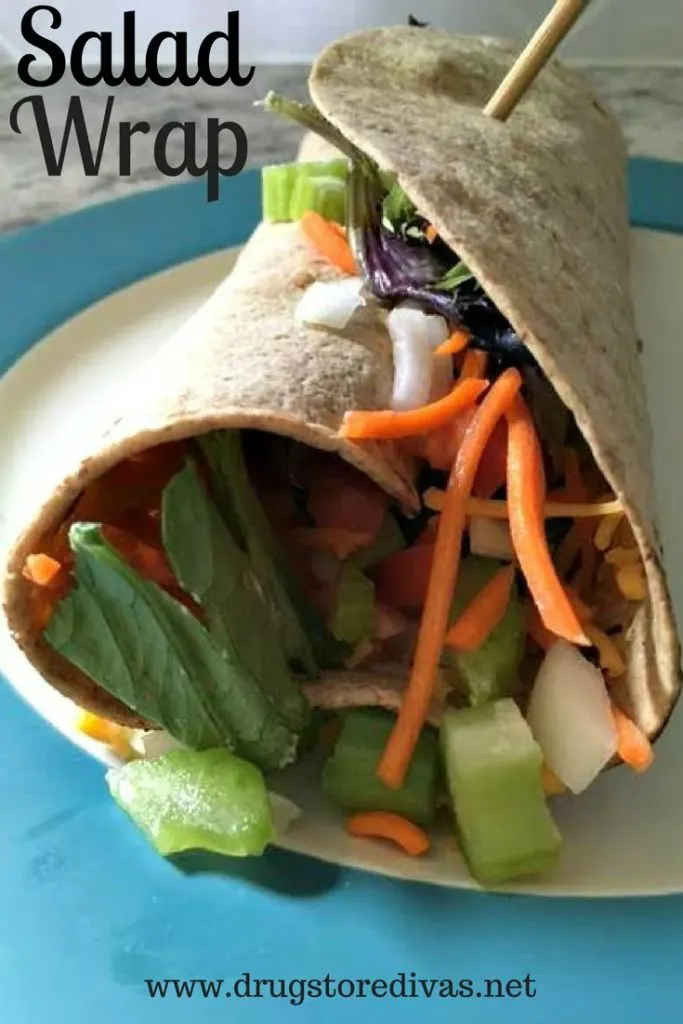 A wrap filled with lettuce, carrots, celery and onions, held together by a toothpick, and the words "Salad Wrap" digitally written above it.