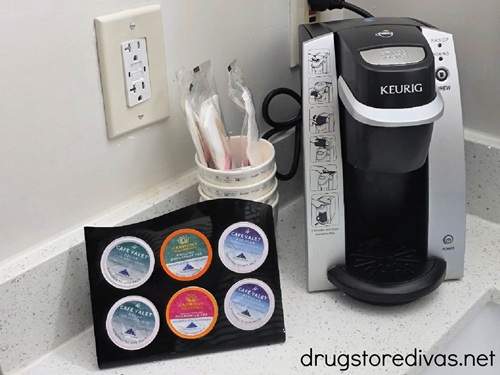 A Keurig coffee maker next to coffee pods and a to go cup in a hotel room.