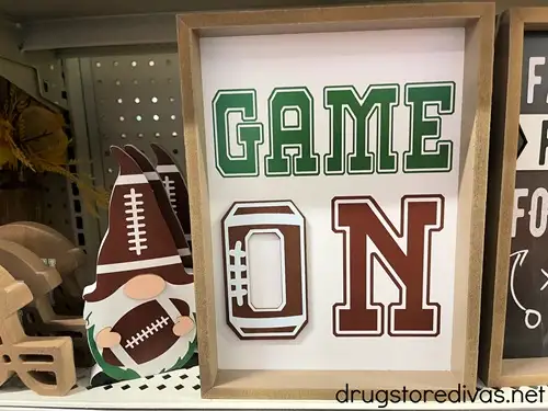 A wooden football gnome next to a sign that says Game On on a shelf in a store.