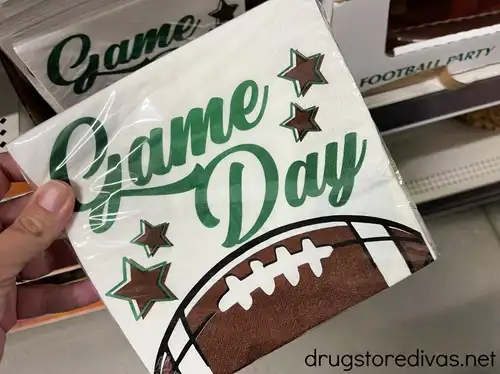 A hand holding napkins with a cartoon football on them that say Game Day.