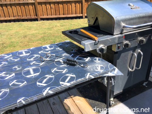 A grill outside with a table with a football tablecloth next to it.