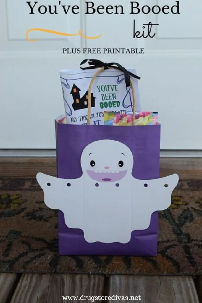 Booing your neighbors this Halloween is simple with this You've Been Booed Kit and free printable from www.drugstoredivas.net. A You've Been Booed kit, which is a purple bag with a ghost on the front filled with candy,