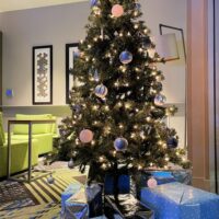 A Christmas tree and gifts on display in a hotel lobby with the words 