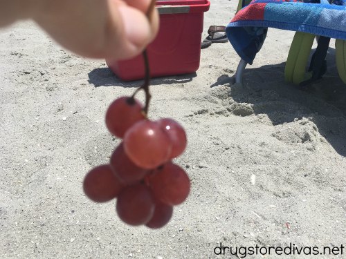 A hand holding grapes at the beach.