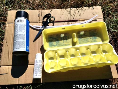 Supplies for egg carton eyeballs, including spray paint, scissors, pipe cleaners, white paint, and an egg carton.