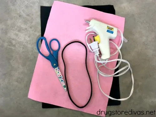 A piece of black felt, a piece of pink felt, a pair of scissors, a headband, and a glue gun.