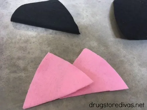 Two pink felt triangles with two pieces of black felt in the background.