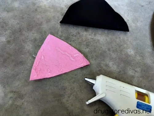 A pink felt triangle with glue on it near a black felt triangle and a glue gun.