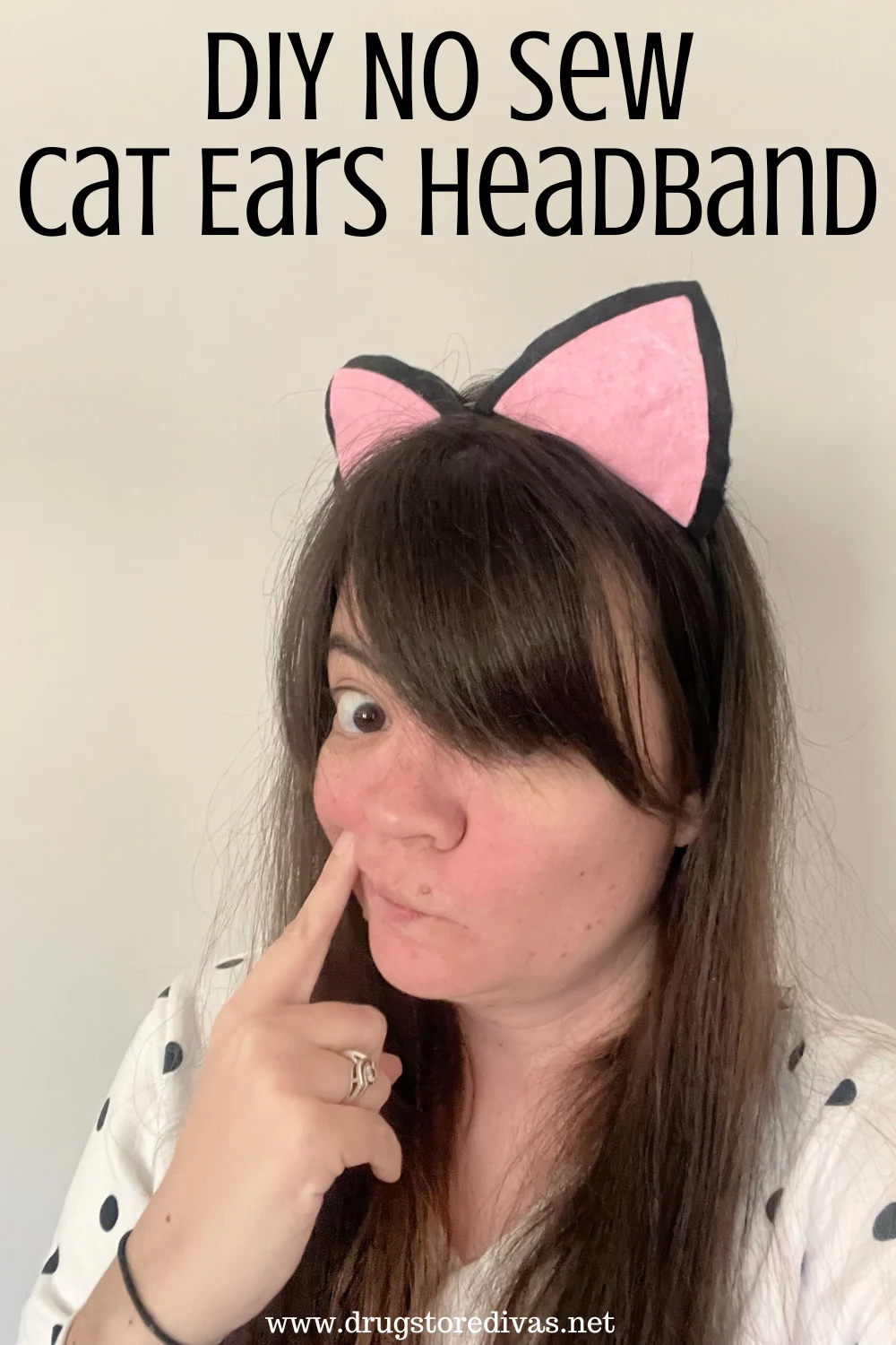 A woman in a white with black polka dot shirt wearing pink and black cat ears with the words 
