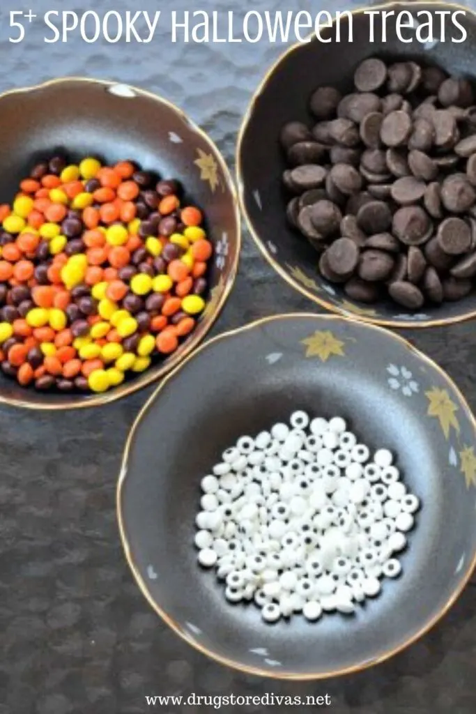 Three bowls, one with Reese's pieces, one with chocolate chips, and one with candy eyeballs, on a glass table.