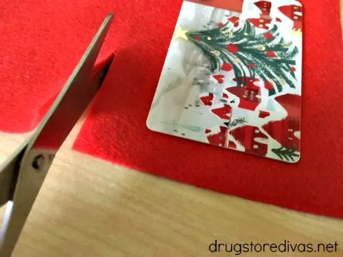 A gift card on red felt that's being cut with scissors.