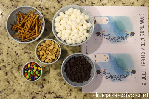 Pretzels, marshmallows, peanuts, chocolate chips, chocolate-covered sunflower seeds, and a printable DIY Snowman Snack Mix printable.