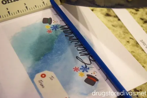 A printable snowman snack mix gift card being cut with a paper trimmer.