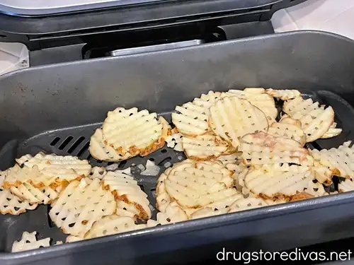 Raw waffle fries in an air fryer basket.