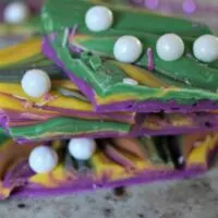 Green, yellow, and purple candy bark, with white sugar pearls, on a pile with beads around it and the words 