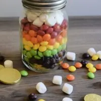 A jar filled with Skittles to look like a rainbow, with gold coins, marshmallows, and Skittles around it with the words 