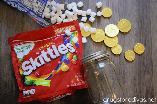 A bag of Skittles, mini marshmallows, gold chocolate coins, and a mason jar.